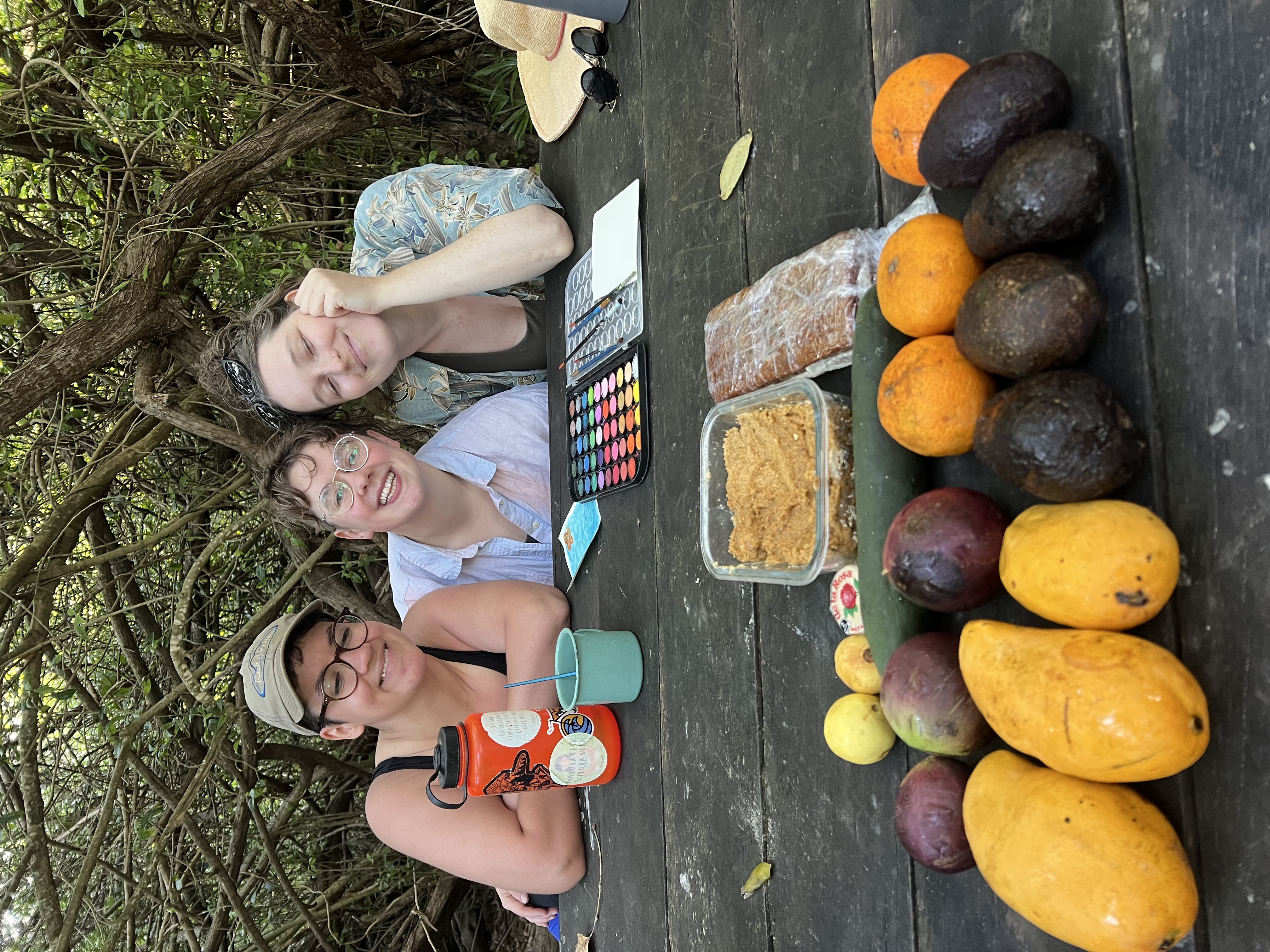 Friends painting together over a picnic spread of fresh fruit during Camp Queerness near Tulum