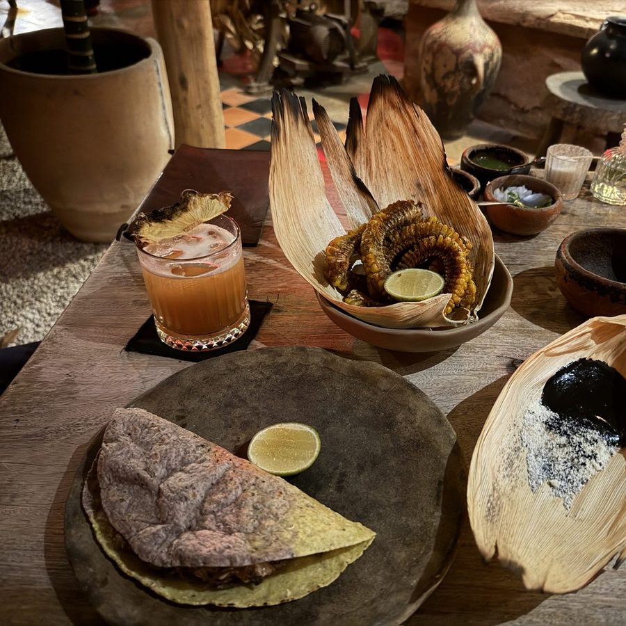 Grilled corn, a cocktail and a blue corn quesadilla on a clay-and-wood table at Negro Huitlacoche in Tulum